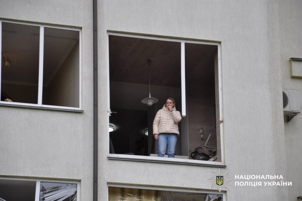 жінка стоїть у пошкодженій від обстрілу багатоповерхівці