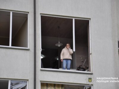 жінка стоїть у пошкодженій від обстрілу багатоповерхівці