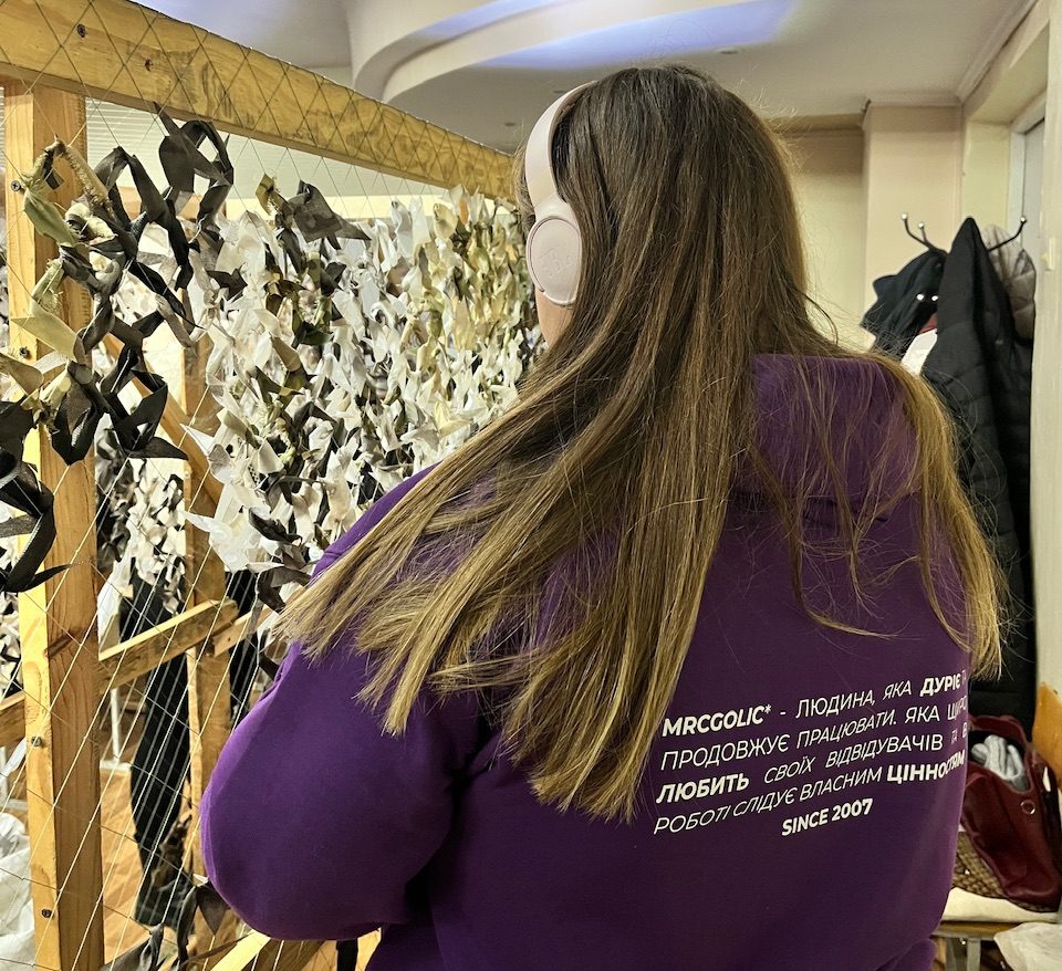 дівчина на фоні рами для плетіння маскувальних сіток